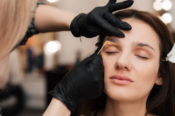 The cosmetologist-brovist corrects and gives shape, plucks out excess hairs in the eyebrows with wax in the beauty salon. Professional facial care