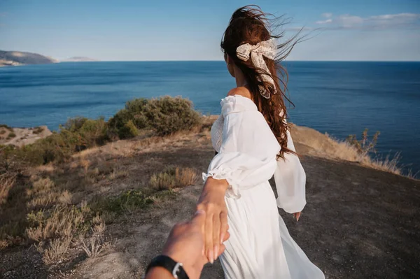 ついて来い。白いドレスの少女が崖に手で男を導く。青い海を見てみろ。風にドレスと髪がなびいている。自由の概念 — ストック写真