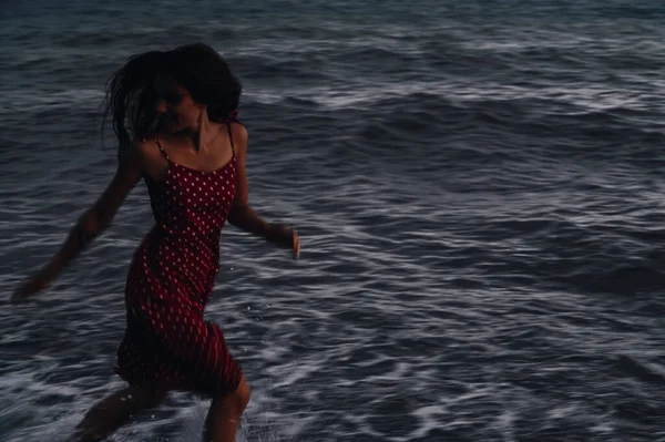 夏の夜に波の海岸線に沿ってドレスを着た若い女の子が走っています. — ストック写真