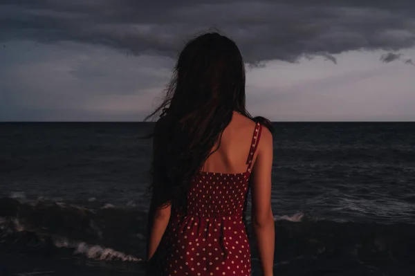 ドレスを着た若い女の子が水の端に立って、夏の夜に海を見ています。自由の概念. — ストック写真