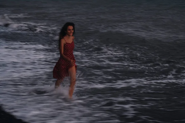 夏の夜にビーチの波に沿ってドレスを着た幸せな若い女の子が走ります. — ストック写真