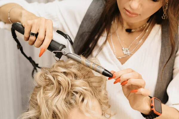 A filmar num salão de beleza. Um cabeleireiro faz um penteado para uma jovem garota de cabelos escuros com a ajuda de um cabeleireiro. — Fotografia de Stock