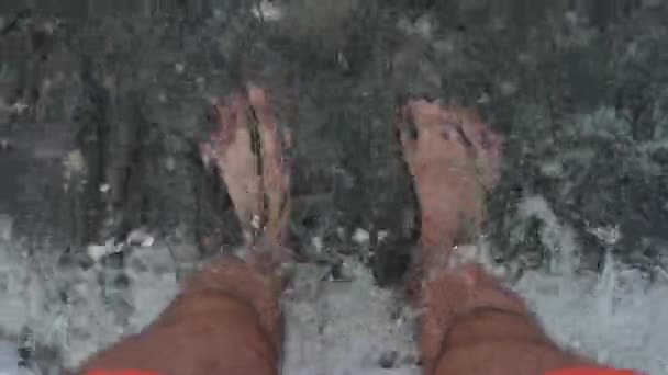 Mens opalone nogi stoją w morzu. Są myte przez fale. Koncepcja relaksu i wakacji letnich. Film w zwolnionym tempie. — Wideo stockowe