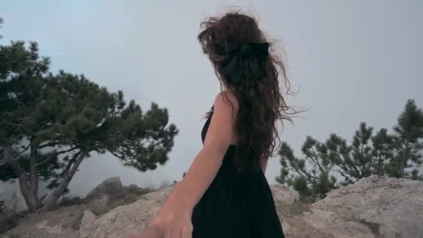 Proszę za mną. Młoda kobieta stoi w pobliżu klifu na klifie na wysokości chmur i trzyma za rękę męskiego podróżnika. Dziewczyna odwraca się do kamery i się uśmiecha. Koncepcja wolności. Autentyczne wideo — Wideo stockowe