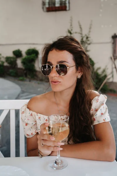 Una giovane donna è seduta in un caffè estivo in una giornata di sole con un bicchiere di vino bianco. Il concetto di ritiro. — Foto Stock