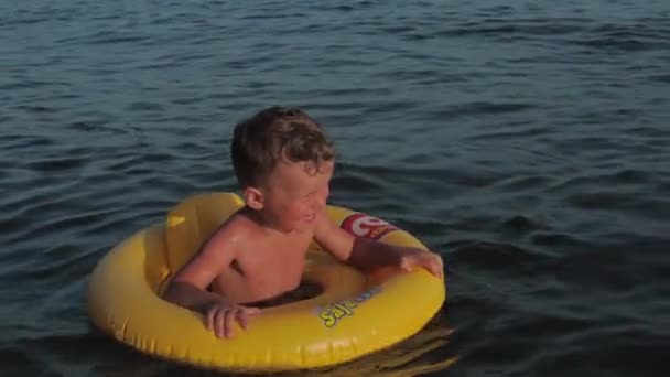 Un enfant garçon dans un cercle de natation jaune dérive sur les vagues dans la mer. L'enfant est heureux et souriant. Vidéo 4k au ralenti et authentique. — Video