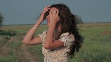Bozkırda güzel bir kız. Yavaş çekim otantik video. Güzel bir genç kız saçını kulağının arkasına saklar. Güçlü bir rüzgar esiyor. Kız gülümsüyor.