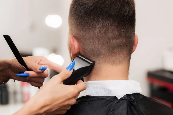 Barbeiro-uma mulher faz um corte de cabelo para um jovem com um clipper. Close-up — Fotografia de Stock