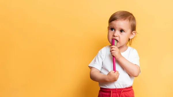 Uma menina loira escova os dentes com pasta de dentes. Fundo amarelo. Um lugar para a tua mensagem. O conceito de higiene dentária. — Fotografia de Stock