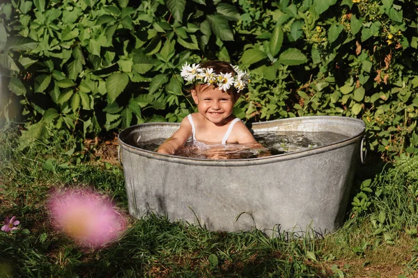 Una niña sonriente se baña en un baño para niños de pie en el jardín, en un día soleado caliente de verano —  Fotos de Stock