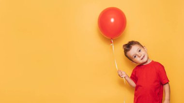 Parlak sarı arka planda izole edilmiş mutlu bir beyaz çocuk elinde kırmızı bir balon tutuyor. Mesajınız ya da ilanınız için bir yer.