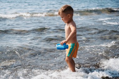 A cute Caucasian boy launches a plastic boat into the sea. Active holidays on the coast