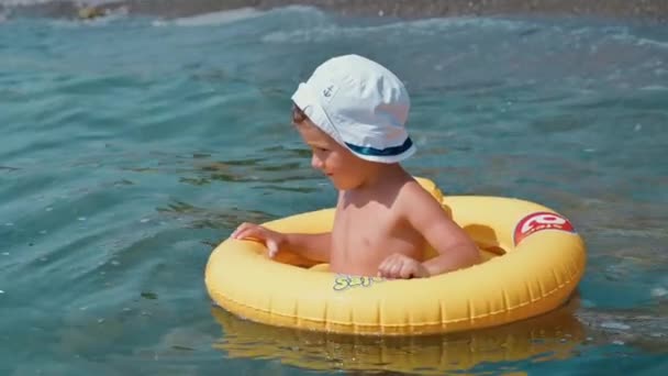 Chłopiec w żółtym kręgu pływackim dryfuje po falach w morzu. Dziecko jest szczęśliwe i uśmiechnięte. Zwolnione tempo i autentyczne wideo 4k. — Wideo stockowe