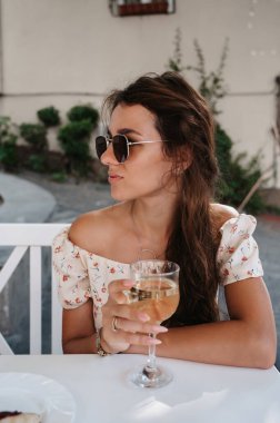 Güneşli bir günde genç bir kadın bir bardak beyaz şarapla bir yazlık kafede oturuyor. Yoksunluk kavramı.