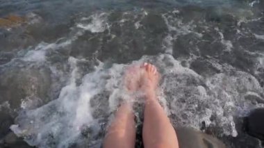 Tanned female legs splashing in the sea. A young woman enjoys time on the beach, the concept of a summer vacation. slow motion video