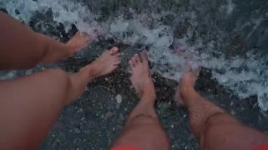 Male and female tanned legs are standing in the sea. They are washed by waves. The concept of family relaxation and summer holidays. Slow motion video