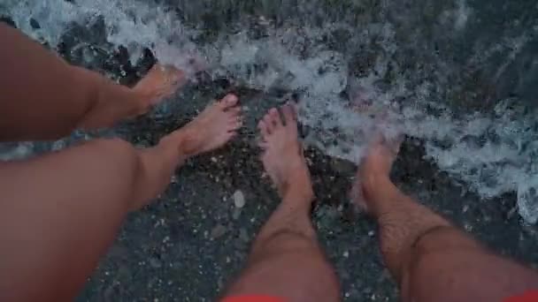 男性和女性晒黑的腿站在海里。它们被海浪冲刷着。家庭放松和暑假的概念。慢动作视频 — 图库视频影像
