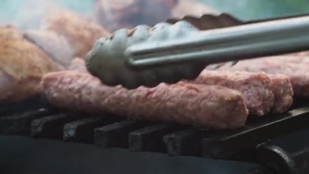Com pinças, ele vira as salsichas na grelha no churrasco. kupaty adquirir uma cor frita — Vídeo de Stock