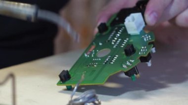 Bir adam tamir atölyesinde lehim yapıyor. Levyeyi lehimleme demiriyle...