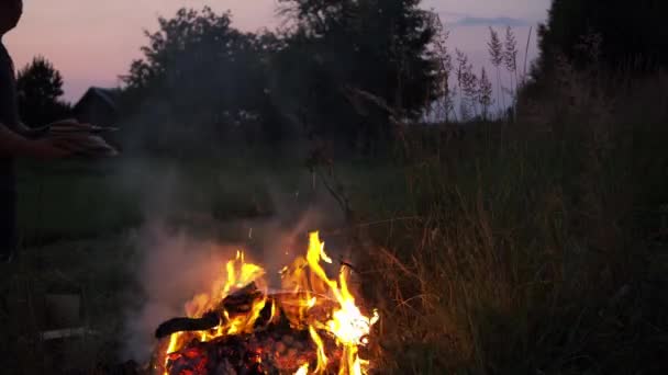 En man kastar gamla tidningar, gamla kläder, träd grenar i elden — Stockvideo