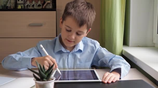 Bir öğrenci bir tabletle kurşun kalemle resim çizer. Mavi gömlekli bir çocuk masada ders çalışıyor. — Stok video