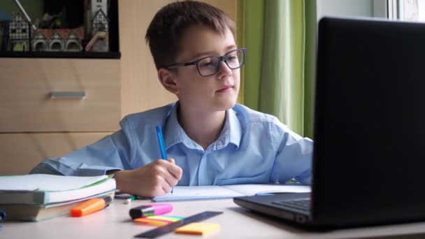 Apprendimento a distanza. uno studente adolescente sta studiando su un computer portatile. annotare una sinossi in un quaderno. seduto a casa alla scrivania. videocorso — Video Stock