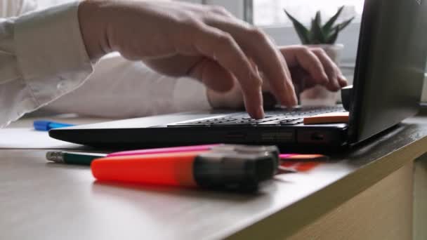 Asztal. Férfiak egy pólóban gépelnek egy laptop billentyűzetén. jegyzetekhez és laptophoz szükséges írási anyagok — Stock videók