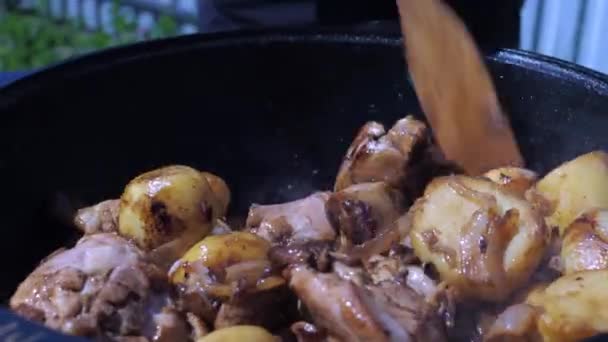 Ruka muže míchá brambory s masem v kotli na ohni. vaření v přírodě — Stock video