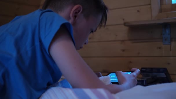 Le garçon est allongé sur le matelas et joue avec le téléphone. esports sur une tablette. il regarde attentivement l'écran — Video