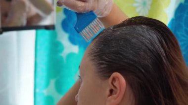 Bir kadın saçını fırçayla boyar. Boyayı köklerine sürüyorlar. Esmer saçların yakın çekimi.