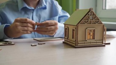 Bir mimar çocuk kontrplaktan yapılmış bir evin modelini topluyor. Gömlekli bir çocuğun elleri. Ev yakın plan.