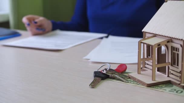 Una donna firma un contratto di mutuo per una casa. c'è una casa in legno sul tavolo, le chiavi della proprietà. familiarizzazione con il contratto di acquisto — Video Stock