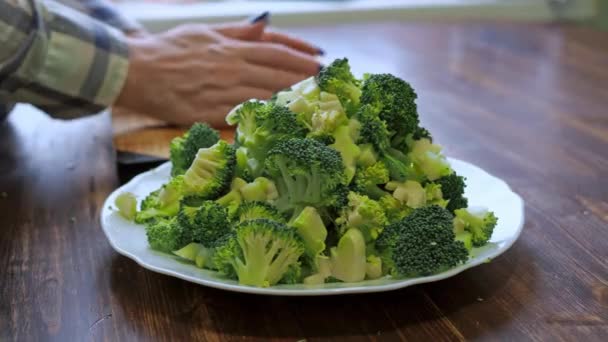 Una donna mette dei broccoli affettati su un piatto. alimentazione sana. una donna in camicia. cottura — Video Stock