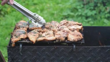 Izgarada tavuk filetosu pişirmek. Aşçı ızgaradaki fileto dilimlerini maşayla çevirir. Arka planda bir yangın yanıyor