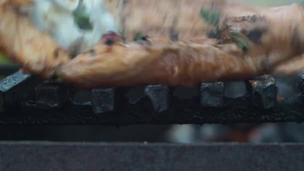 Cuire le filet de poulet sur le gril. le cuisinier tourne les tranches de filet sur le gril avec des pinces. un feu brûle en arrière-plan — Video