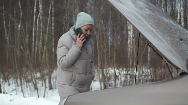 Μια γυναίκα στο τηλέφωνο καλεί για βοήθεια, ένα αυτοκίνητο χάλασε έξω από την πόλη το χειμώνα. επικίνδυνη παγωνιά. κυκλοφοριακή κατάσταση. Κλήση γερανού — Αρχείο Βίντεο