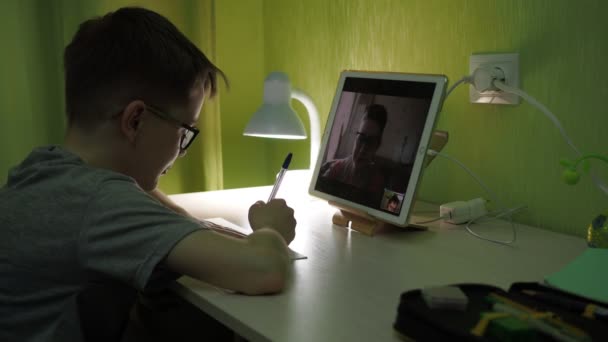 Online les. De jongen beantwoordt de vragen van de leraren. schrijft de samenvatting op in een notitieboekje — Stockvideo