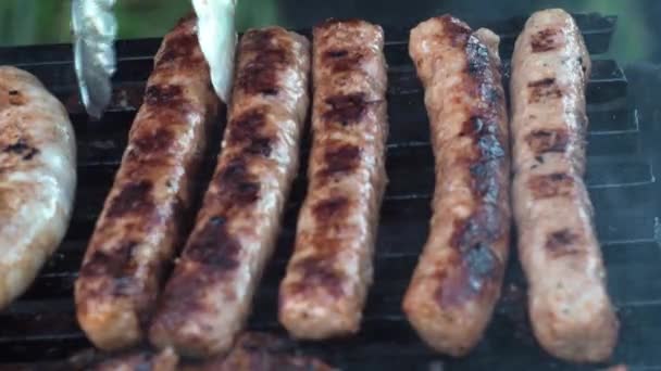 Korv grillas på kol som tillagas på en grill. Vänd på den med tång — Stockvideo