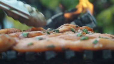 Izgarada tavuk filetosu pişirmek. Aşçı fileto dilimlerini ızgaraya koyar. Ortasına odaklan. Arka planda bir yangın yanıyor