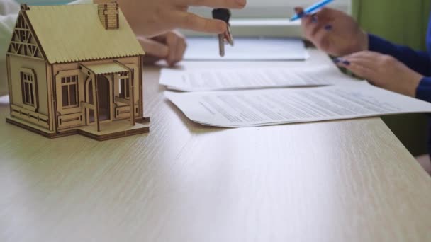 Une femme signe un contrat d'hypothèque immobilière. transfert de clé. il y a une maison en bois sur la table, les clés de la propriété — Video