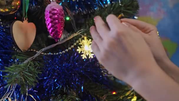 Gros plan des mains d'enfants décorant un sapin de Noël avec un jouet de cerf sur un fond de lumières festives lumineuses. les enfants décorent le sapin de Noël — Video