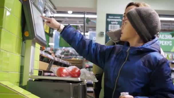 Eine Frau mit Kind wiegt in einem Geschäft Tomaten auf einer Waage. eine Vitrine mit Produkten. Supermarkt Lebensmittelgeschäft, Einzelhandel — Stockvideo