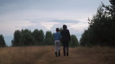 Aile ormanda yürümeye başladı. Arkadan bak. İki kişi. Çocuklu bir anne ormanda bir patika boyunca yürüyor.