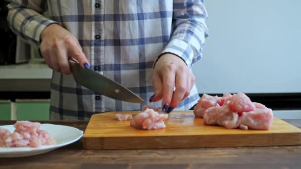 Una mujer corta un filete de pollo en una tabla de cortar madera. cocinar en la cocina. primer plano de las manos con un cuchillo y una mesa — Vídeo de stock