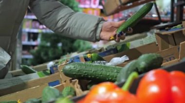 Ürünlerle dolu bir vitrin. Bir kadın çantaya salatalık koyar. süpermarket, perakende