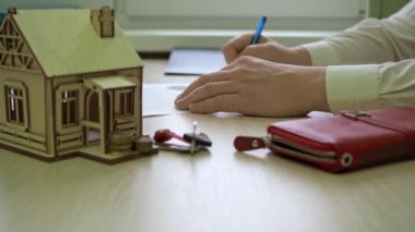Adam kontratı imzalıyor. Masanın üzerinde ahşap bir ev var, evin anahtarları.