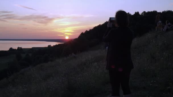 Een vrouw neemt een zonsondergang op haar telefoon. rode zonsondergang op de achtergrond. Wandeltochten. de schoonheid van de natuur — Stockvideo