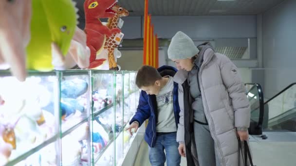Een vrouw met een tienerzoon die naar een showcase kijkt met speelgoed in een winkel. zacht speelgoed. een familiebezoek aan de winkel — Stockvideo