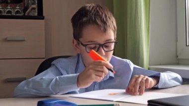 Mavi tişörtlü bir genç not defterine mesaj rehberi çiziyor. Yazı malzemeleri. Bir masa. ev dersleri