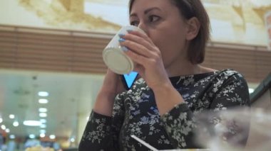 Masadaki bir kadın kahve içiyor. Bir kafede otururken telefonla konuşuyor.